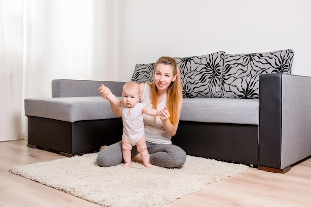Feliz joven madre jugando con su bebé en el suelo cerca del sofá