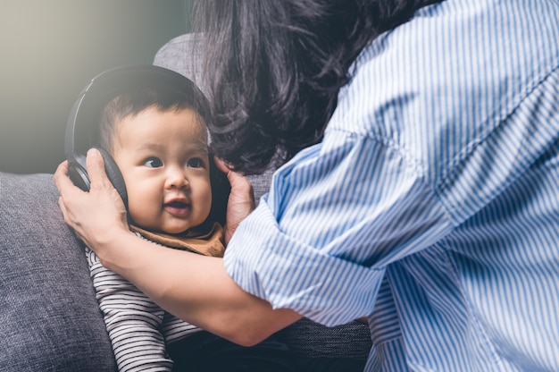 Feliz joven madre usa auriculares a su hijo o niño. Concepto de familia.