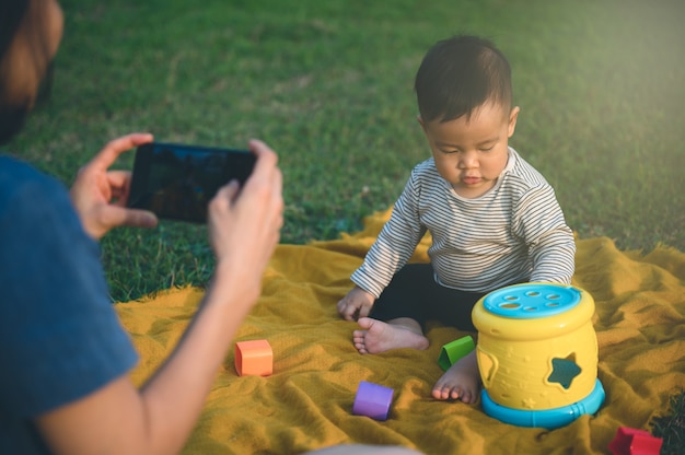 Feliz joven madre usa un teléfono inteligente o un teléfono móvil y toma una foto con su hijo o hijo para la memoria. Concepto de familia.