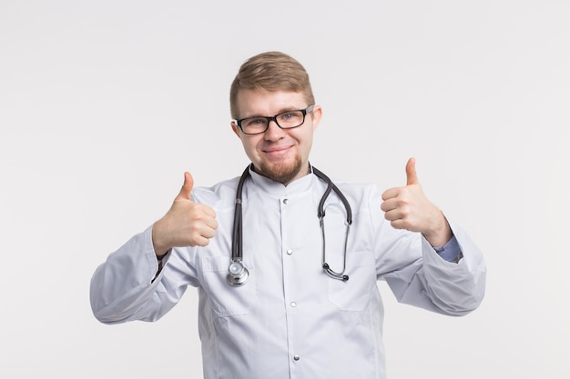 Feliz joven médico blanco en estudio con pulgar hacia arriba con estetoscopio