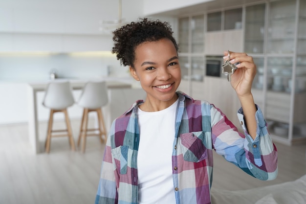 Feliz joven mestiza celebrando la reubicación en un nuevo hogar mostrando la llave del primer apartamento propio