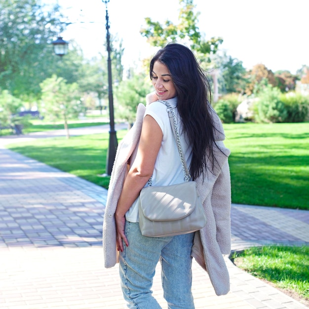 Feliz joven morena al aire libre vestida con abrigo de piel blanca falsa y jeans