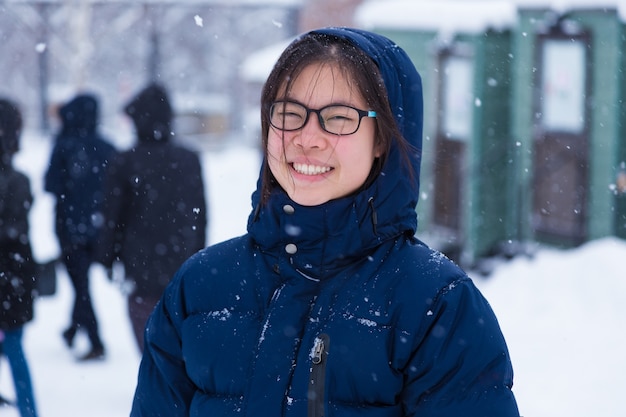 Feliz joven mujer adolescente asiática disfruta de estar afuera durante la nieve del invierno