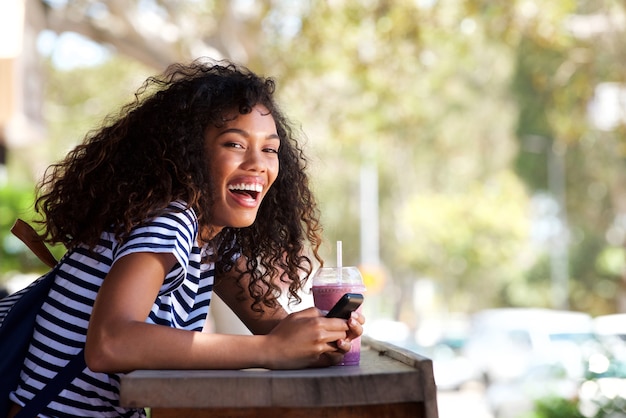 Feliz joven mujer afroamericana con teléfono móvil en el café