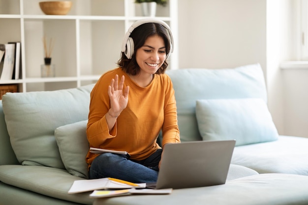 Feliz joven mujer árabe en auriculares haciendo videollamadas en casa