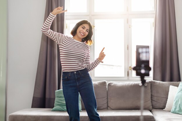 Feliz joven mujer árabe bailando en cámara mientras graba video en casa