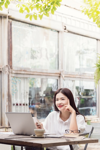 Feliz joven mujer asiática disfrutando de su café mientras usa su computadora al aire libre