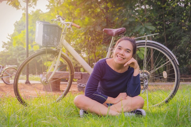 Feliz joven mujer asiática sentada con bicicleta blanca vieja. en el parque.