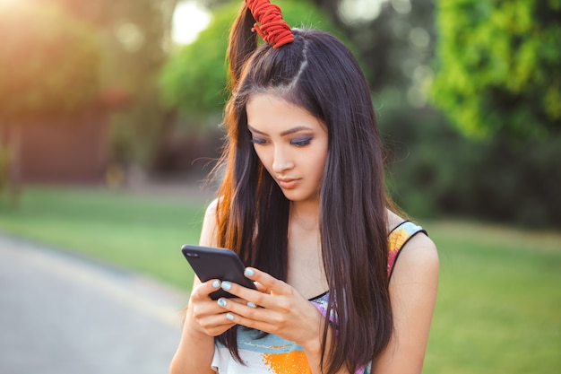 Feliz joven mujer asiática con smartphone de pie en la calle