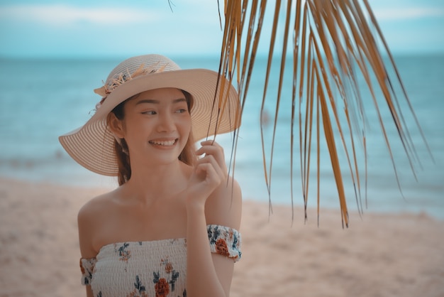 Feliz joven mujer asiática con sombrero caminando y relajarse en la playa de arena con felicidad.