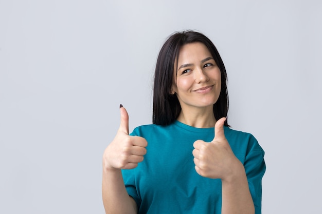 Feliz joven mujer caucásica en una camiseta azul haciendo pulgar hacia arriba signo y sonriendo Buen trabajo respeto