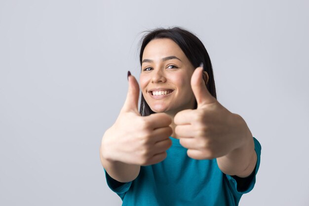 Feliz joven mujer caucásica en una camiseta azul haciendo pulgar arriba signo y sonriendo Buen trabajo