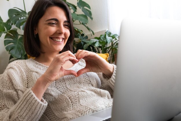 Feliz joven mujer caucásica haciendo forma de corazón con las manos durante una videollamada en línea usando una computadora portátil Espacio de copia Concepto de amor y tecnología