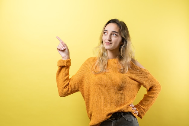 Feliz joven mujer caucásica con un suéter amarillo apuntando con el dedo.
