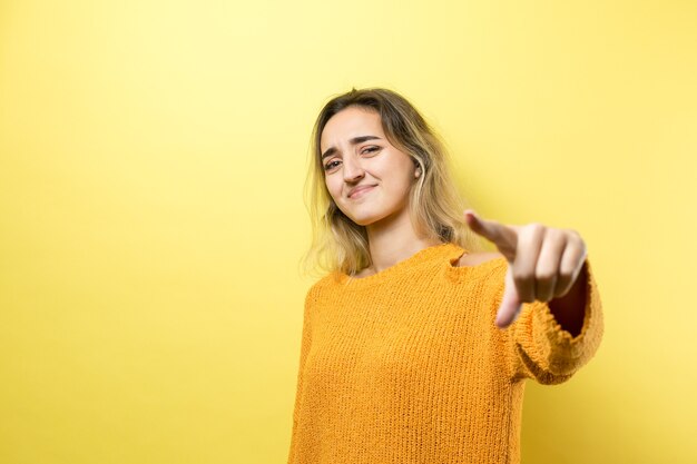 Feliz joven mujer caucásica en un suéter naranja apuntando con el dedo lejos