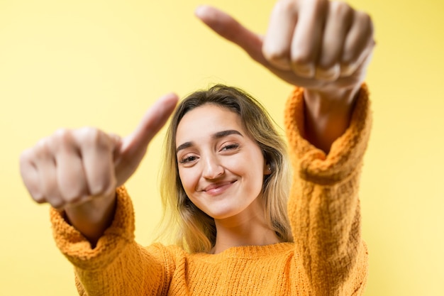 Foto feliz joven mujer caucásica en un suéter naranja haciendo pulgar arriba signo y sonriendo