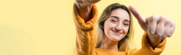 Feliz joven mujer caucásica en un suéter naranja haciendo pulgar arriba signo y sonriendo