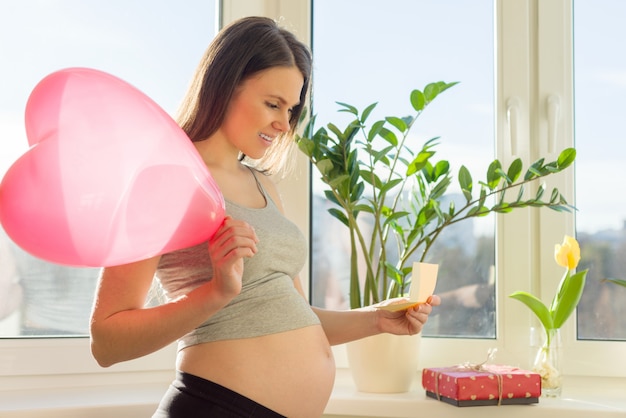 Feliz joven mujer embarazada con caja de regalo y globo de corazón