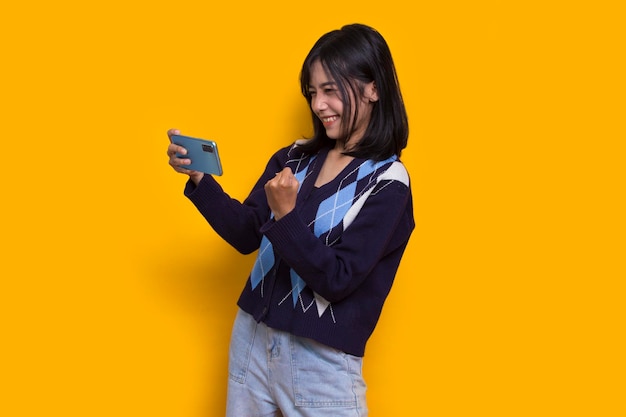 feliz joven mujer hermosa asiática usando teléfono móvil aislado sobre fondo amarillo