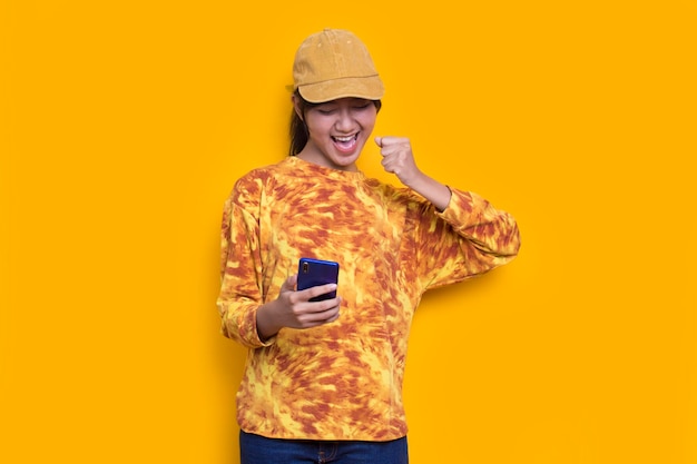 feliz joven mujer hermosa asiática usando teléfono móvil aislado sobre fondo amarillo