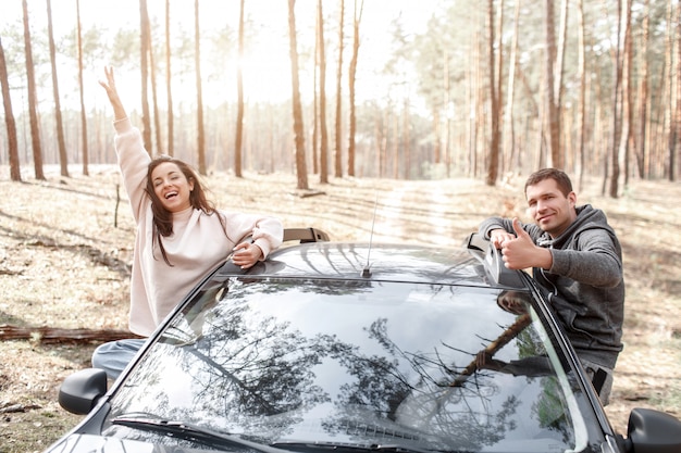 Feliz joven mujer y hombre salieron de la ventana de un automóvil. Viajando en coche por el bosque. Viaje de campo. Vacaciones en coche