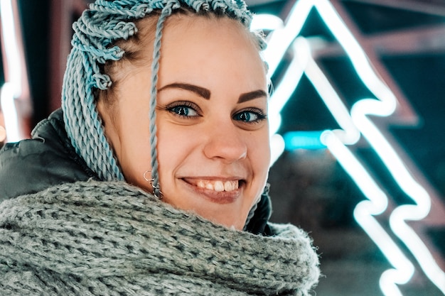 Feliz joven mujer moderna con coletas o rastas sonriendo mirando a la cámara con el telón de fondo de la iluminación fluorescente