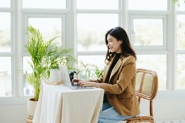 Feliz joven mujer de negocios asiática está usando una computadora portátil en línea en casa Pequeños empresarios