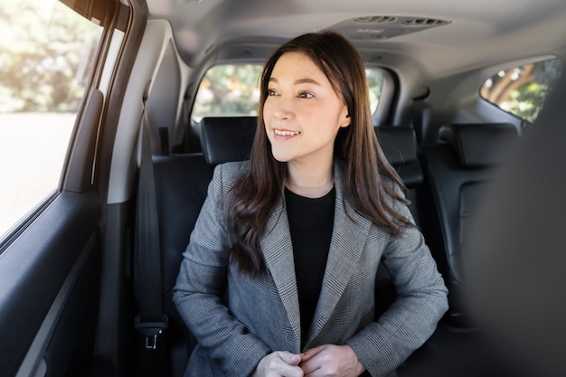 Feliz joven mujer de negocios pensando y mirando por la ventana mientras está sentado en el asiento trasero del coche