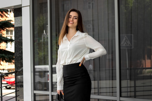 Feliz joven mujer de negocios en uniforme blanco y negro sonríe al aire libre