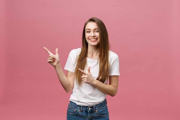 Feliz joven mujer de pie y apuntando el dedo aislado sobre fondo rosa