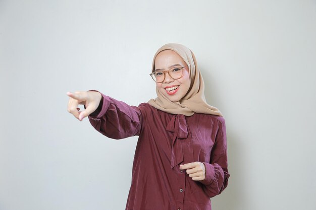 Feliz joven musulmana asiática con anteojos apuntando hacia adelante sobre un fondo blanco aislado