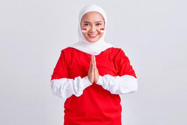 Feliz joven musulmana asiática con camiseta blanca roja saludando a celebrar el día de la independencia de Indonesia el 17 de agosto aislada de fondo blanco