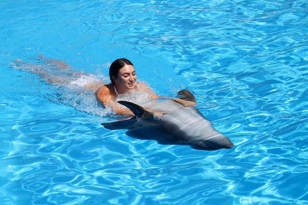 Feliz joven nada con delfines en agua azul.