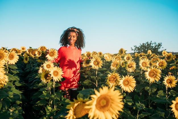 Feliz joven negra caminando en un campo de girasol