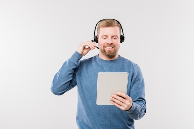 Feliz joven operador en auriculares mirando la pantalla táctil mientras consulta a clientes en línea de forma aislada