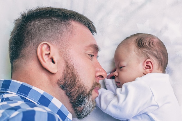 Feliz joven padre barbudo con bebé recién nacido acostado en la cama cara a cara, concepto de crianza, día del padre