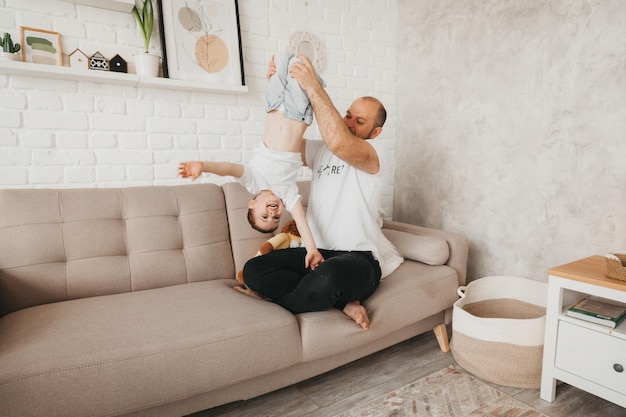 Feliz joven padre caucásico en el sofá en la sala de estar jugando con un pequeño hijo de preescolar