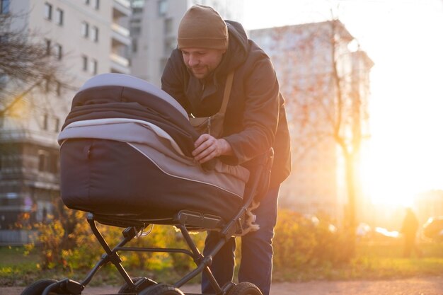 Feliz joven padre con cochecito durante el paseo por la naturaleza en el parque