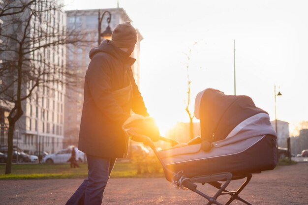 Feliz joven padre con cochecito durante el paseo por la naturaleza en el parque