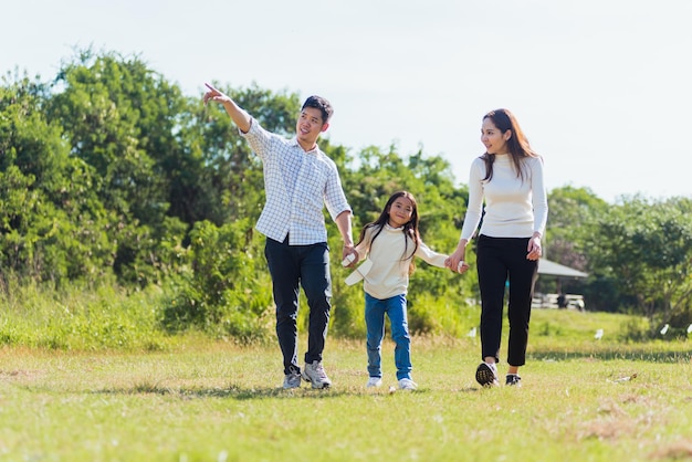 Feliz joven padre de familia asiático, madre e hijo niña divirtiéndose y disfrutando al aire libre caminando por la calle juntos en un parque natural verde en un día soleado de verano