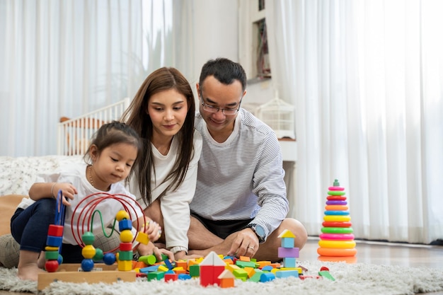 Feliz joven padre y madre y una pequeña hija jugando con bloques de madera de juguete sentados en el suelo en la sala de estar paternidad familiar y concepto de personas con juguetes de desarrollo