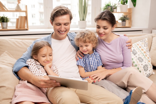 Feliz joven padre sosteniendo la tableta mientras su esposa y dos niños lindos sentados junto a él