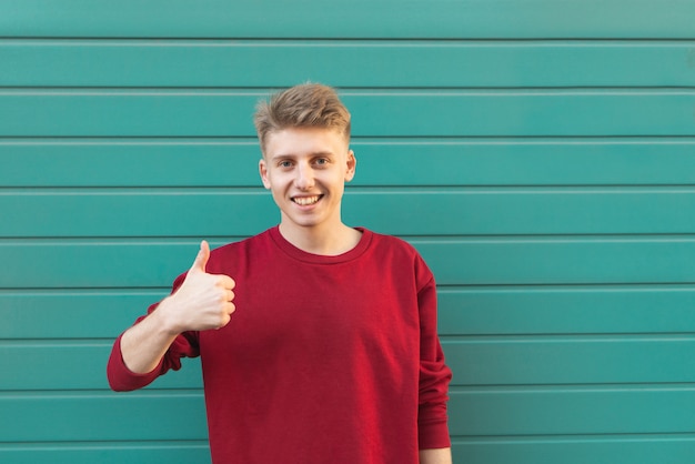 Feliz joven parado en turquesa y mostrando un pulgar hacia arriba.