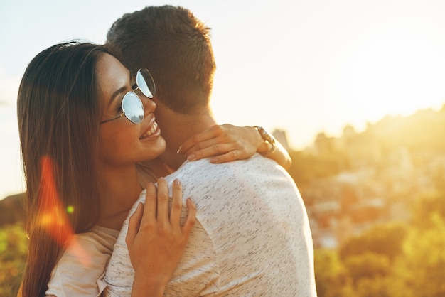 Feliz joven pareja amorosa abrazándose y sonriendo mientras pasa tiempo al aire libre