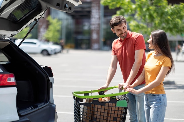 Feliz joven pareja amorosa haciendo compras juntos de pie en coche