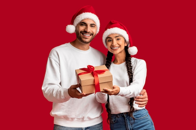 Feliz joven pareja árabe con sombreros de Santa con caja de regalo en las manos