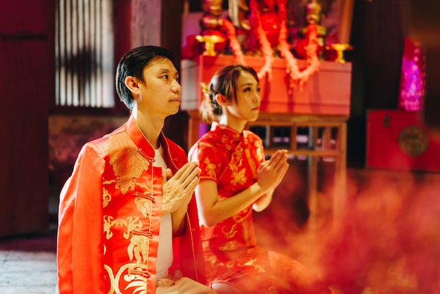 Feliz joven pareja asiática amor en vestidos tradicionales chinos rezando en el templo chino