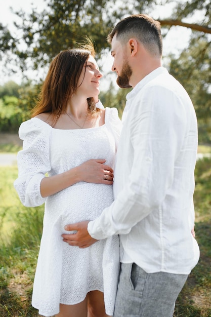 Feliz y joven pareja embarazada abrazando en la naturaleza