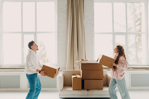 Feliz joven pareja familiar, hombre y mujer, sostiene cajas de cartón en un nuevo hogar, concepto de entrega en movimiento