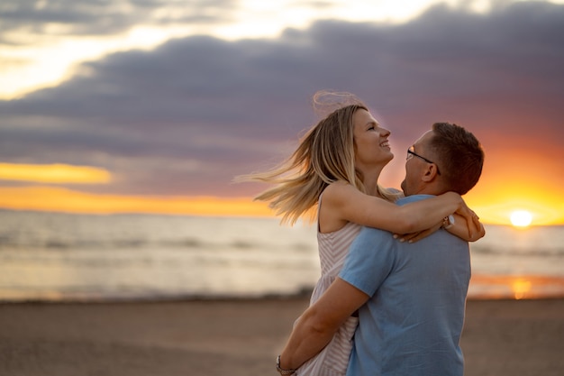 Feliz joven pareja hermosa caucásica en la puesta de sol en la playa en verano Hermoso cielo de fondo